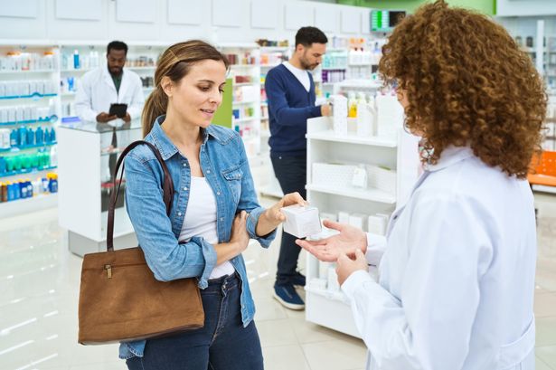 Female customer talking with pharmacist, holding medicine box in hand. They are standing in pharmacy.